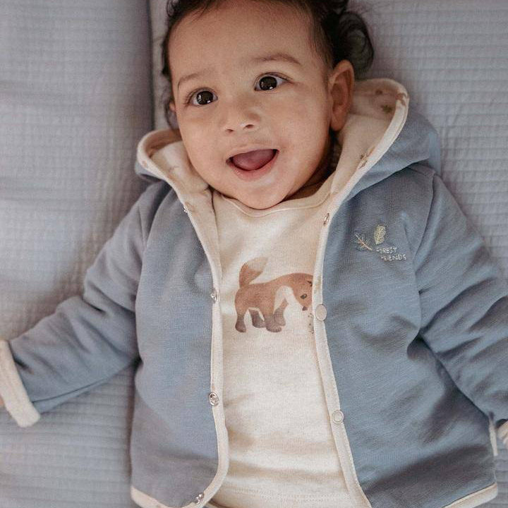 Lächelndes Baby trägt die Little Dutch Wendejacke Stone Blue