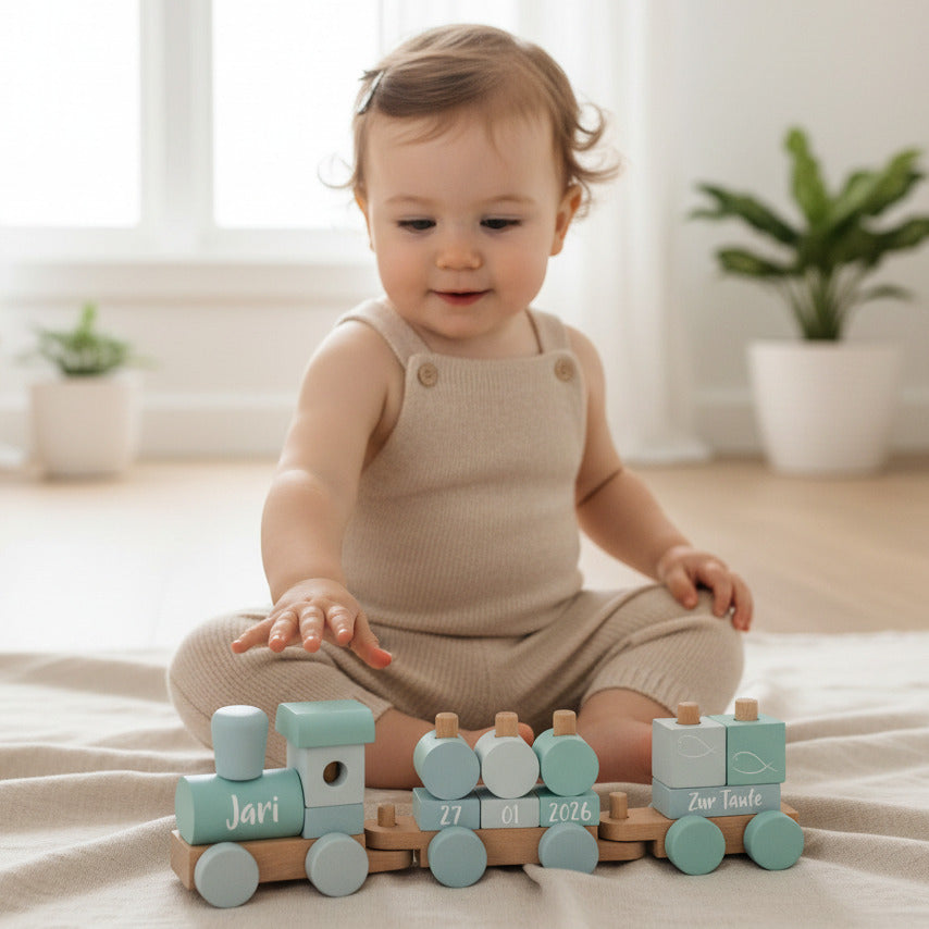 Baby spielt mit blauem personalisiertem Holzzug zur Taufe mit Name und Taufdatum