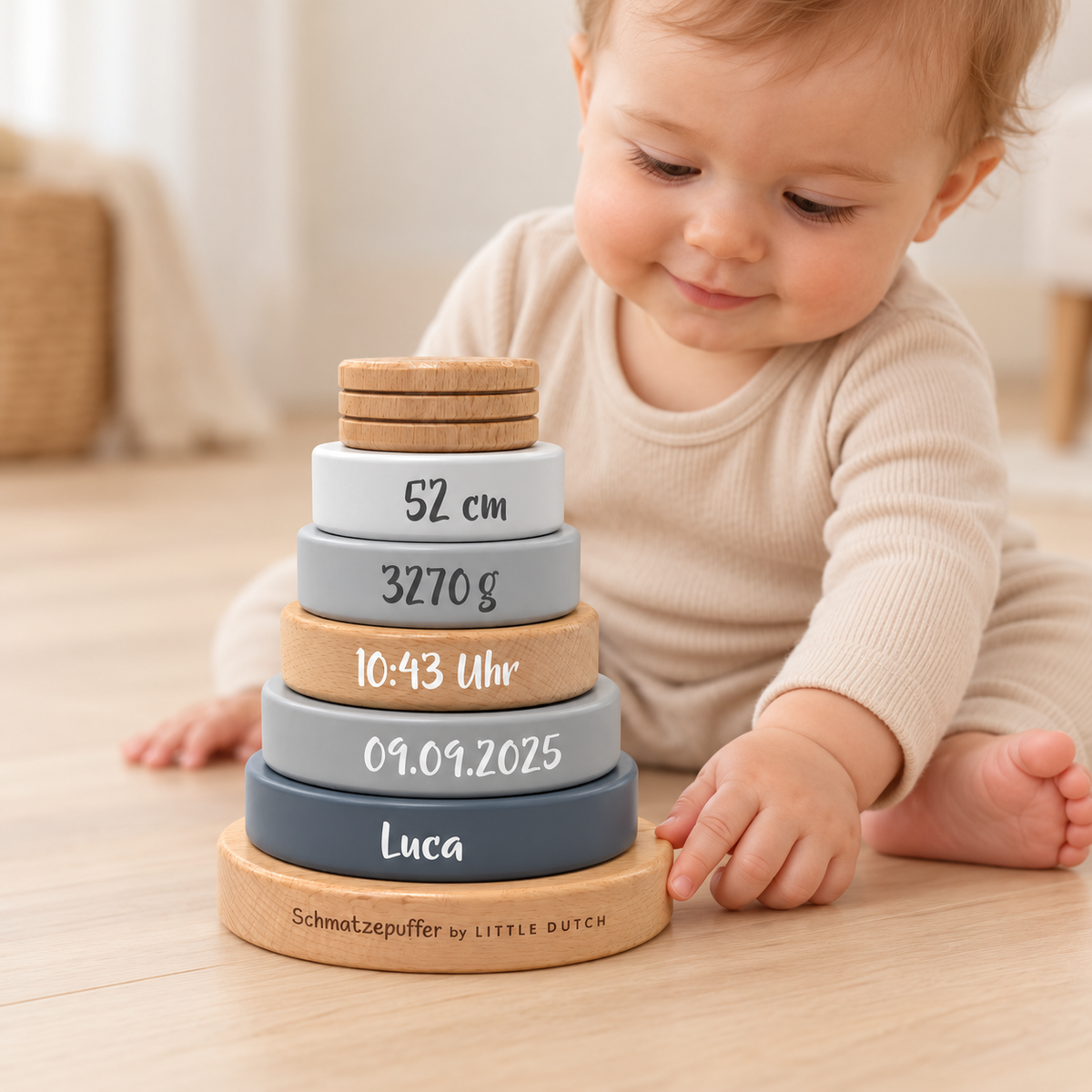 Baby berührt den Holzfuß eines personalisierten Stapelturms in Grau und Naturholz mit Name Luca, Geburtsdatum, Uhrzeit, Gewicht und Größe.